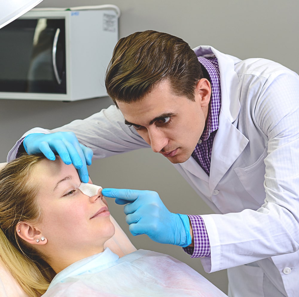 Facial plastic surgeon preparing patient for secondary rhinoplasty procedure Surgeon discussing revision rhinoplasty procedure with patient pre-op