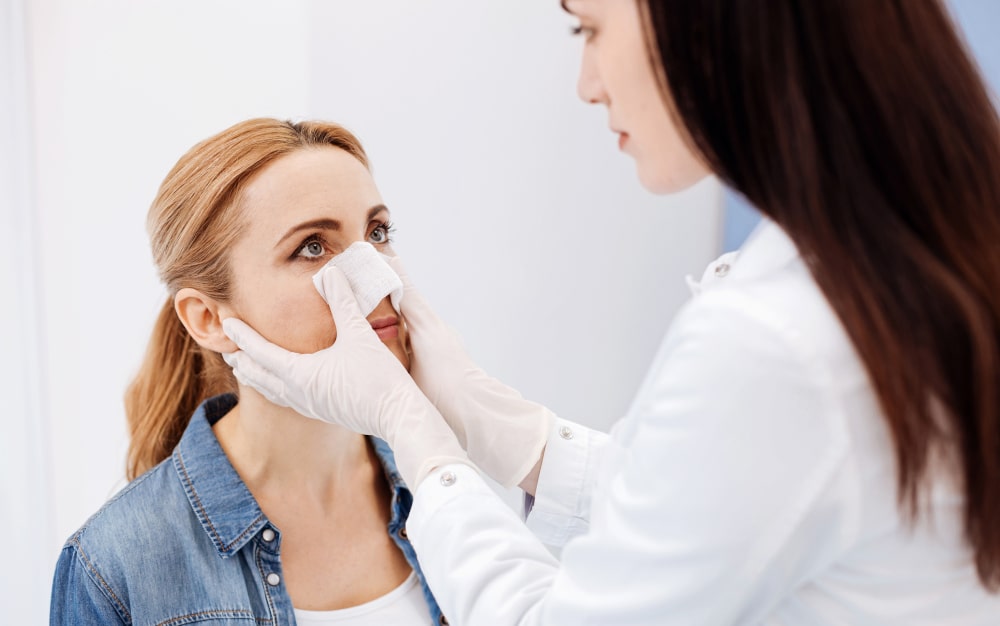 Female surgeon applying dressing after revision rhinoplasty in Canada Female plastic surgeon applying nasal dressing to patient after revision rhinoplasty